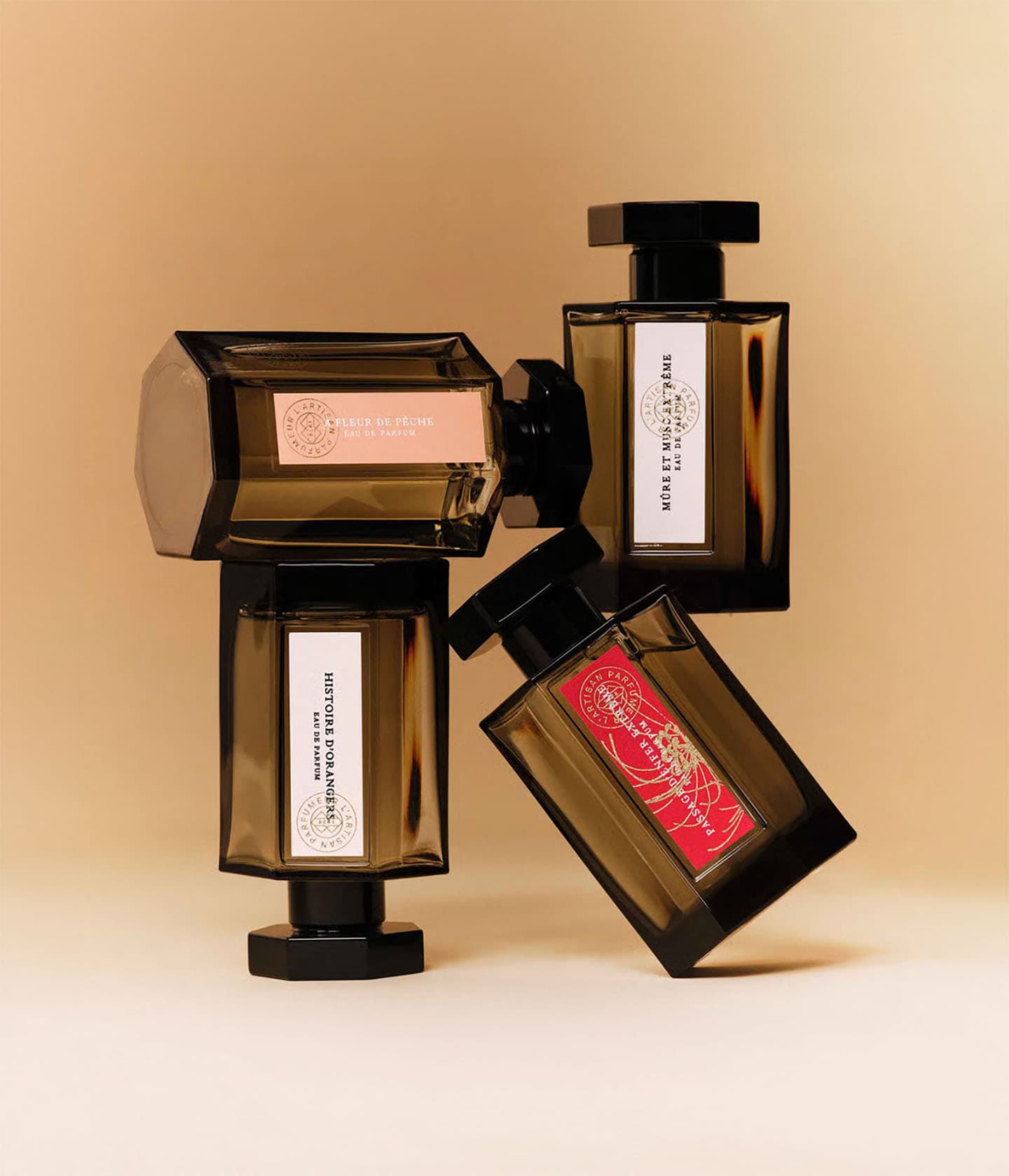 L'Artisan Parfumeur La Collection, vier Flakons übereinander gestapelt vor warmem Beige
