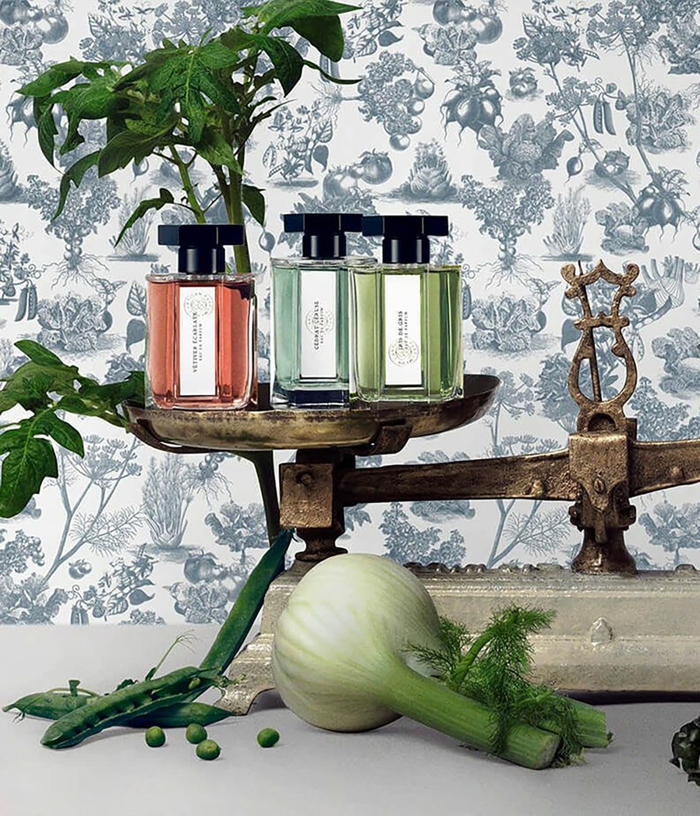 L'Artisan Parfumeur Le Potager, drei Flakons auf einer alten Waage zwischen Fenchel und Erbsen
