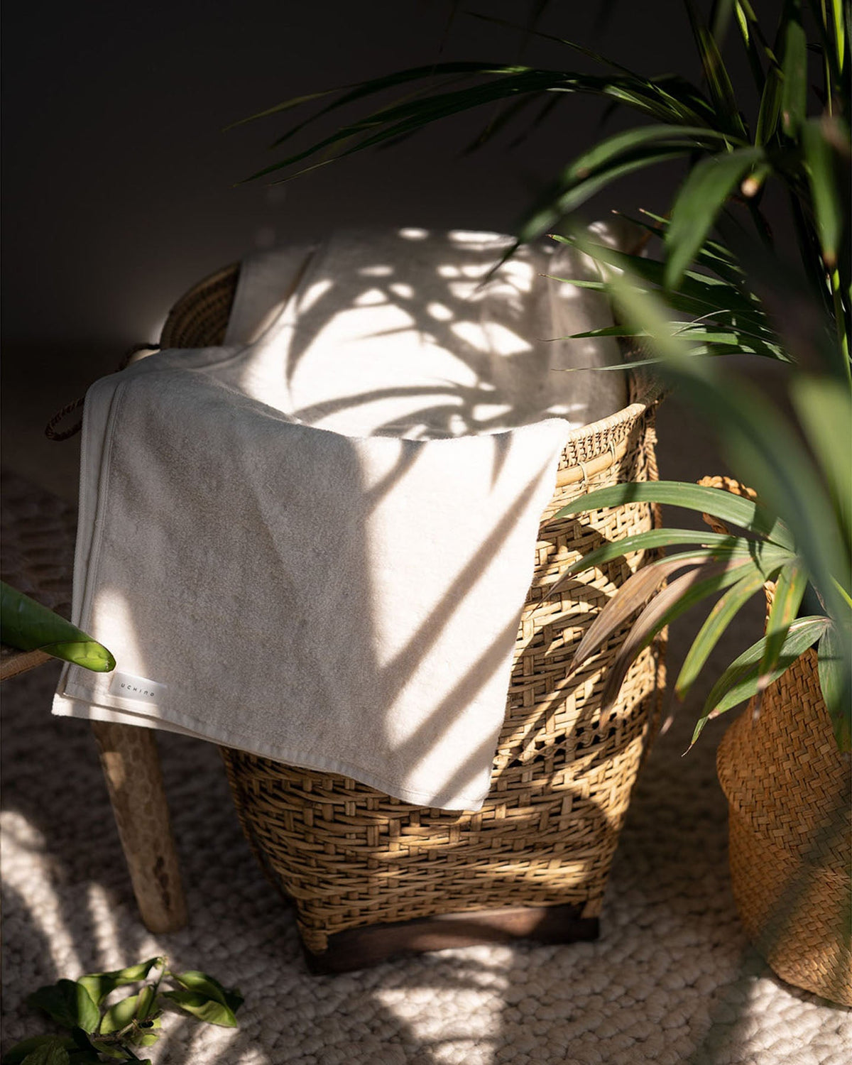 Uchino Handtuch über einem Rattankorb neben Palmblättern