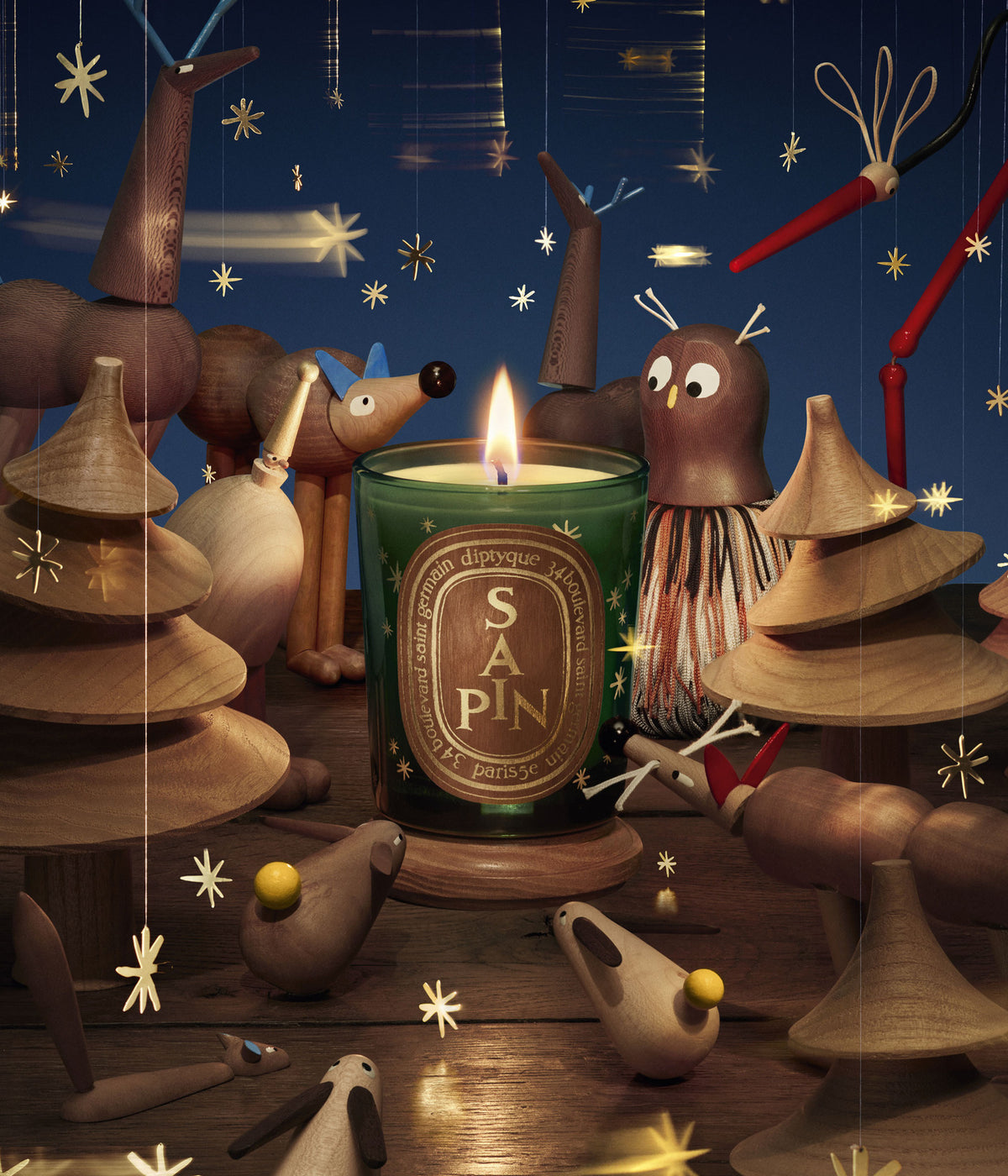 Diptyque Duftkerze Sapin Limited Edition brennend zwischen Holzfiguren