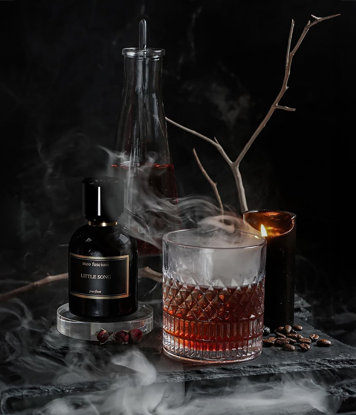 Meo Fusciuni Extrait de Parfum Little Song neben einem Whiskyglas, Kerze und Zweigen im Rauch
