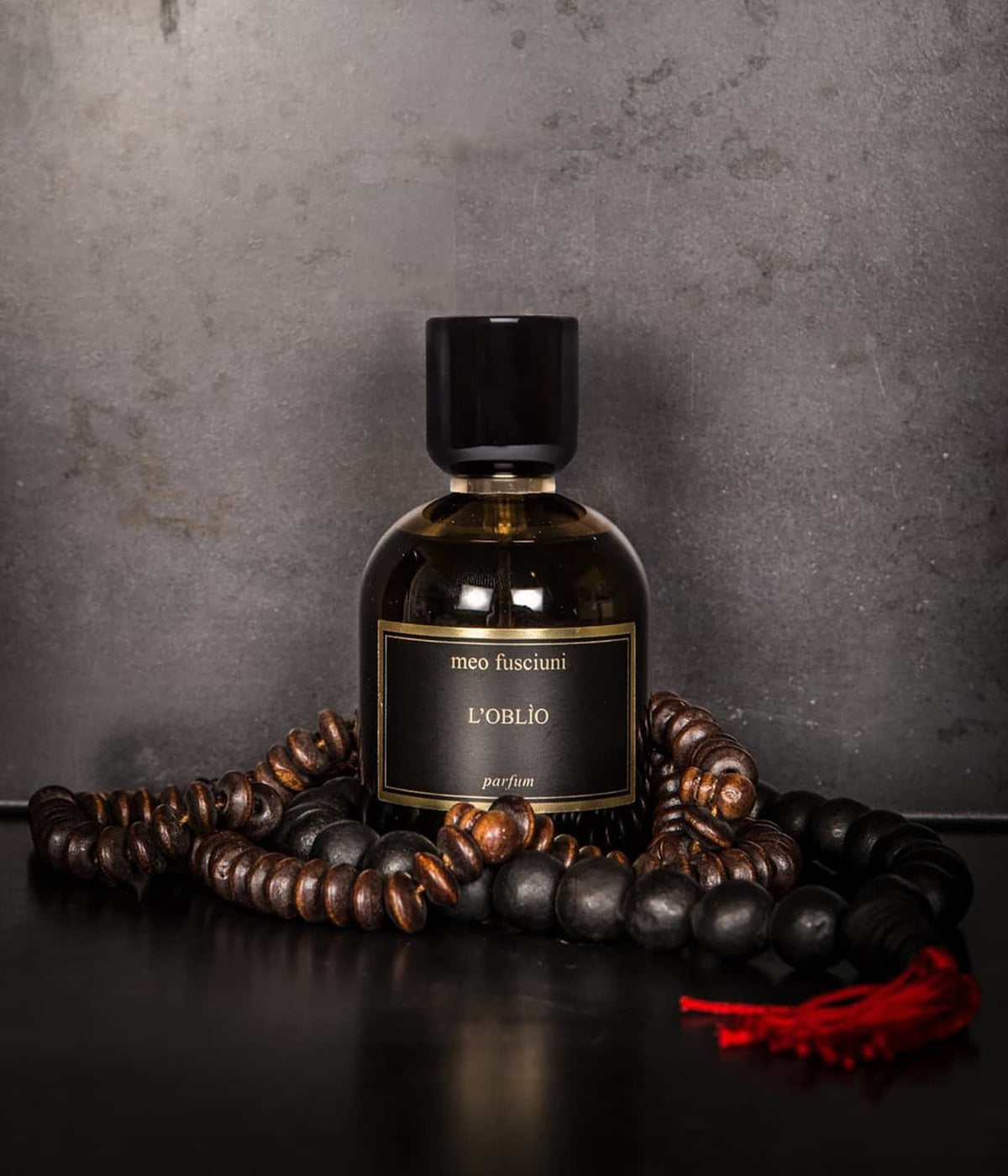 Meo Fusciuni Extrait de Parfum L’Oblio neben einer Holzperlenkette mit roter Quaste