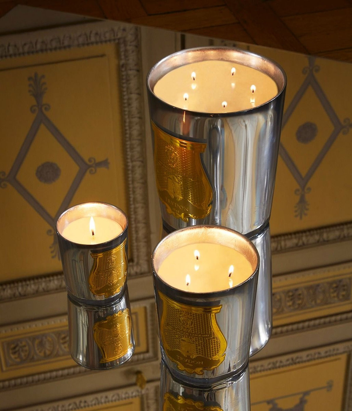 Trudon Duftkerzen Cabinet des Miroirs brennend auf einem Spiegel vor vergoldeter Wandvertäfelung