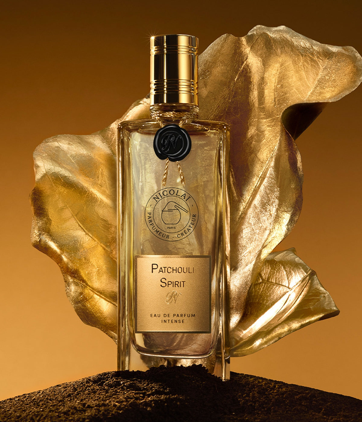 Nicolaï Eau de Parfum Patchouli Spirit in front of a golden leaf on dark soil