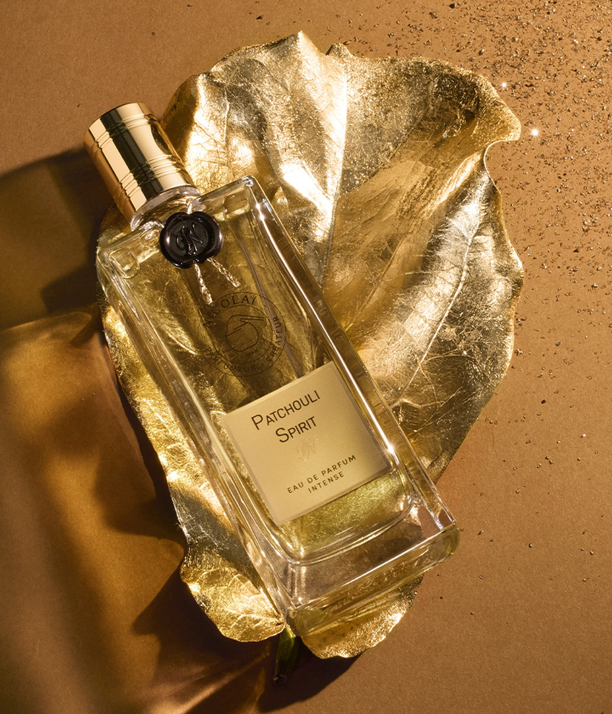 Nicolaï Eau de Parfum Patchouli Spirit lying on a golden leaf against an ochre background