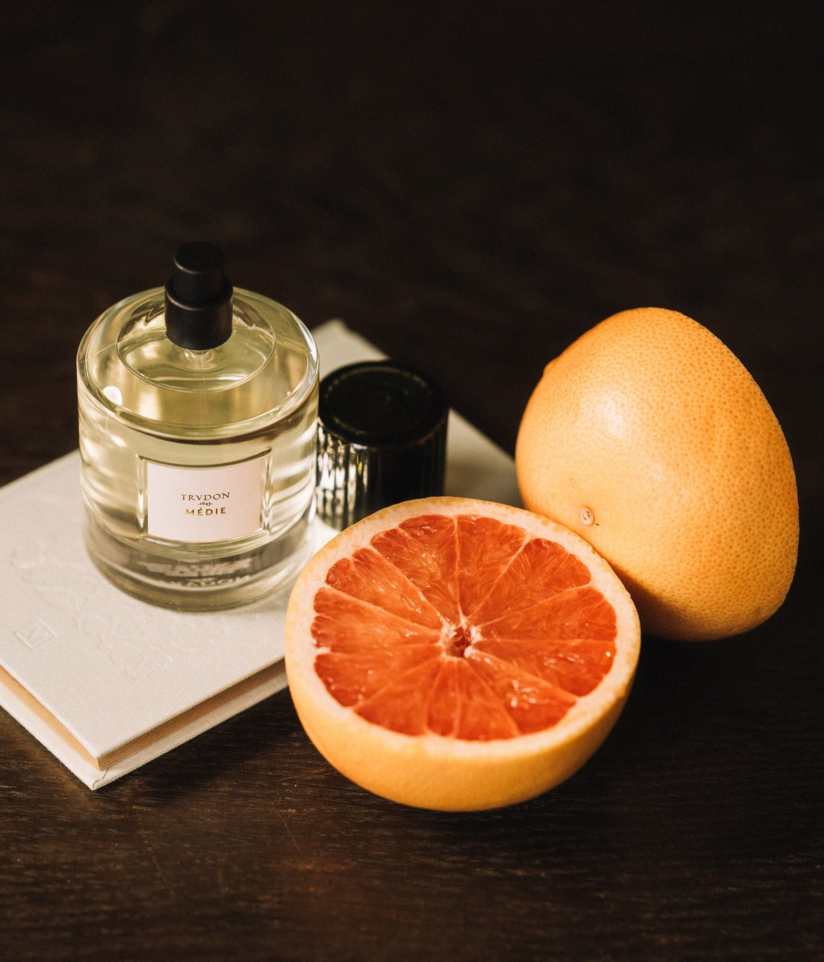 Trudon Eau de Parfum Médie neben einer aufgeschnittenen Grapefruit auf einem Buch